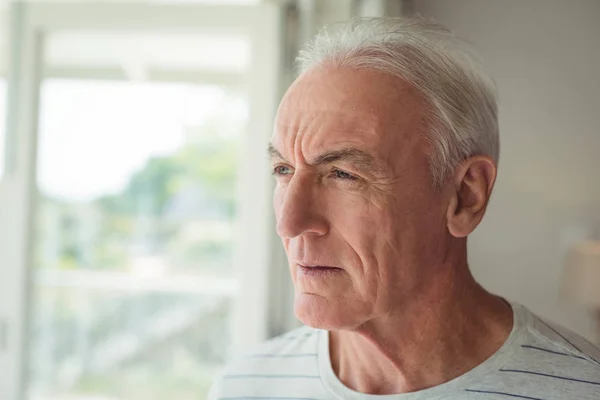 Pensativo hombre mayor de pie junto a la ventana — Foto de Stock