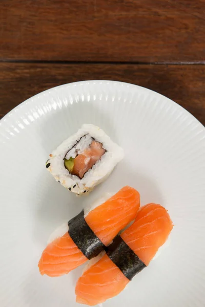 Nigiri och uramaki sushi serveras i vita runda plattan på träbord — Stockfoto