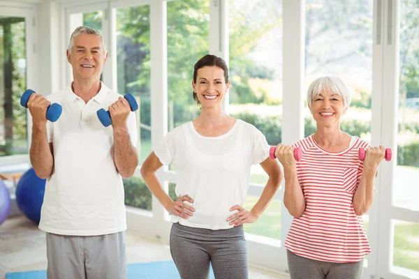 Portrait de formatrice debout avec un couple de personnes âgées tout en faisant de l'exercice avec haltère — Photo