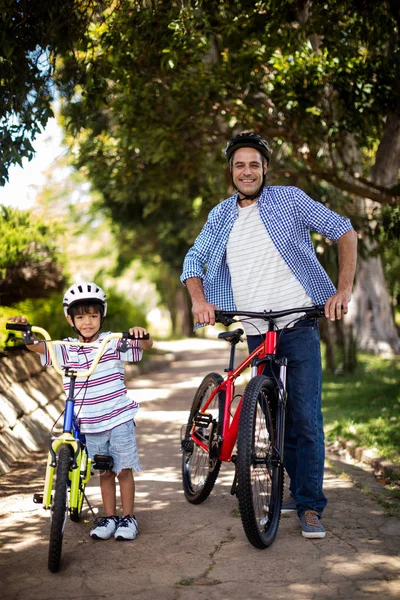 Портрет отца и сына, стоящих с велосипедом в парке — стоковое фото