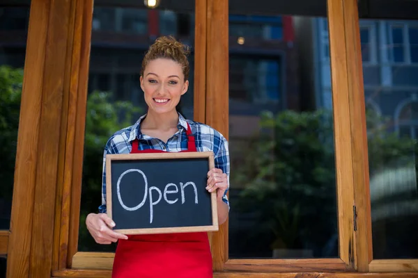 Cameriera sorridente in piedi con cartello aperto fuori caffè — Foto Stock