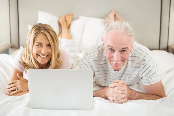 Retrato de pareja sonriente acostada en la cama y usando laptop — Foto de Stock