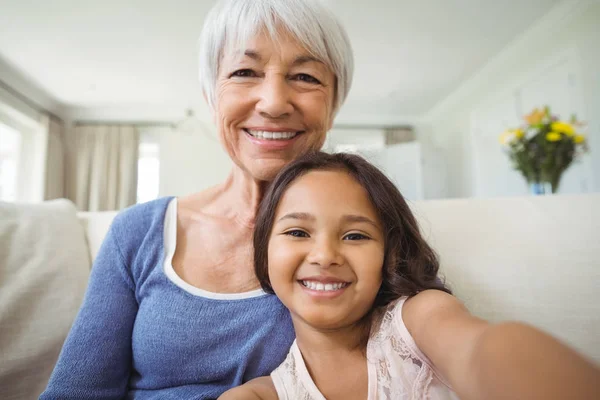 Porträtt av leende barnbarn och mormor sitter på soffan i vardagsrummet — Stockfoto