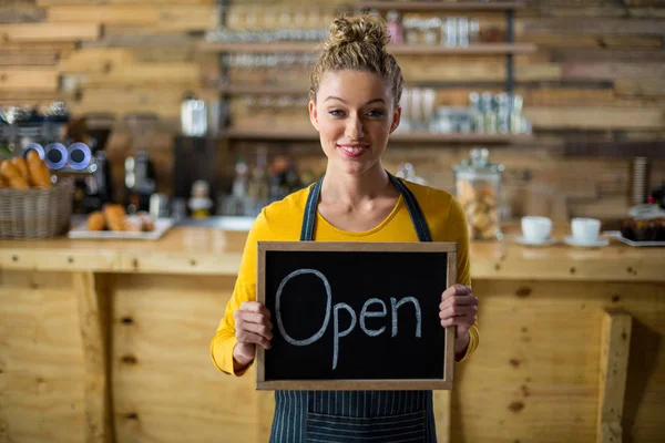 Smiling waitress standing with open sign board in cafe — Stock Photo, Image