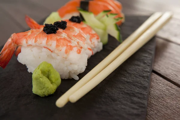 Nigiri sushi servido com pauzinhos em ardósia de pedra preta na mesa de madeira — Fotografia de Stock