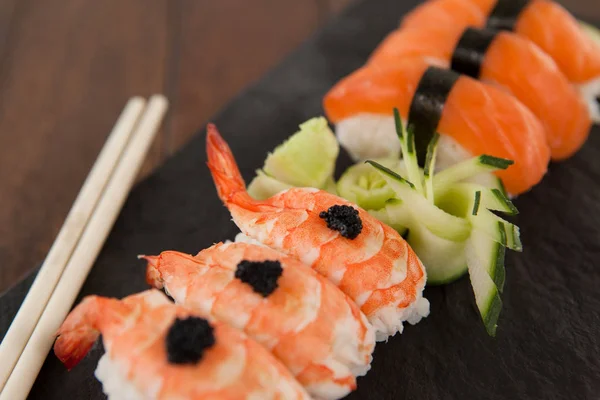 Nigiri sushi servido com pauzinhos em ardósia de pedra preta na mesa de madeira — Fotografia de Stock