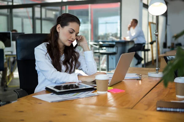 Business executive talking on mobile phone while using laptop at desk — Stock Photo, Image