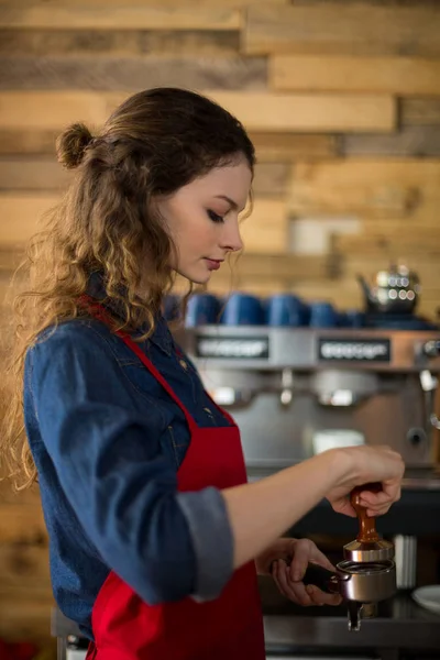 Serveuse utilisant un tampon pour presser du café moulu dans un portable — Photo