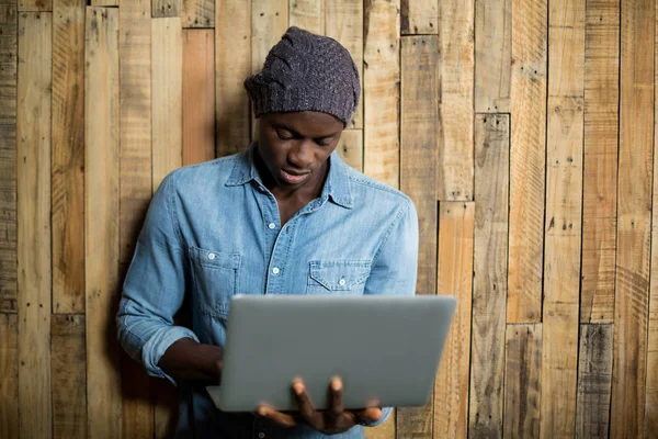 Człowiek za pomocą laptopa drewnianą ścianę — Zdjęcie stockowe