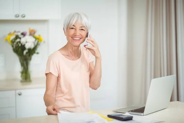 Portret van senior vrouw praten op mobiele telefoon in de keuken — Stockfoto