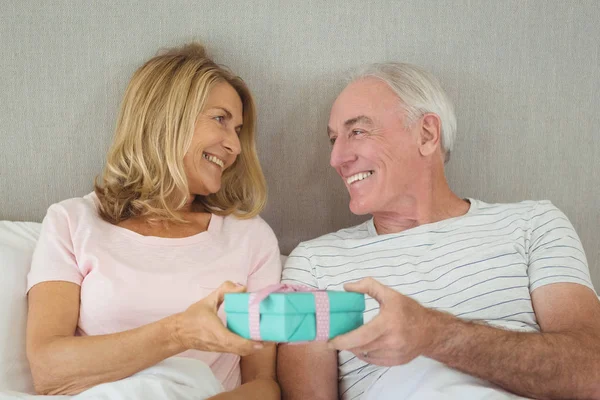 Senior couple holding gift box on bed — Stock Photo, Image