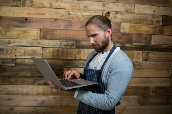 Uppmärksam servitör använder laptop mot trävägg — Stockfoto