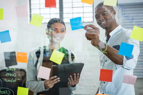 Compañeros de negocios discutiendo sobre notas adhesivas en vidrio — Foto de Stock