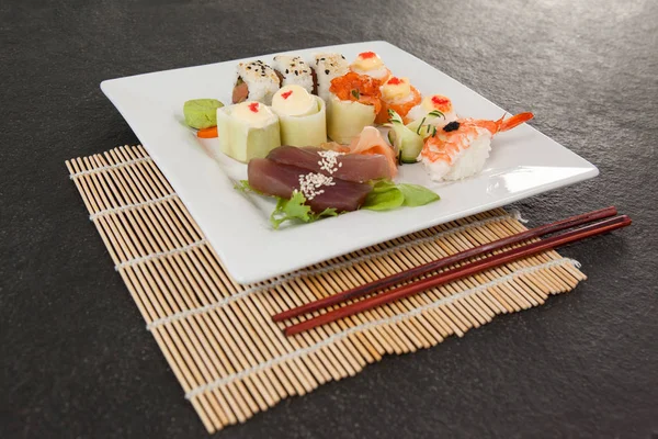 모듬된 스시 세트 젓가락으로 초밥 매트에 흰색 접시에 봉사 — 스톡 사진