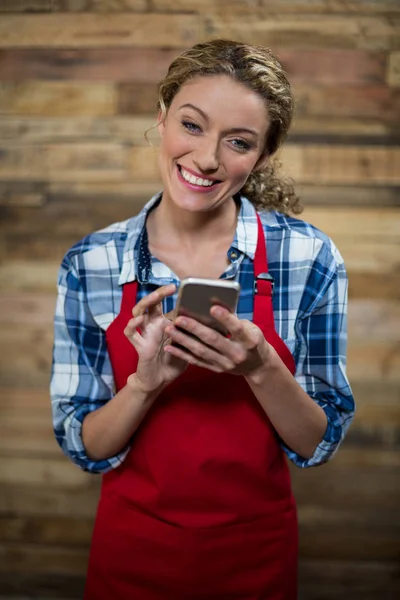 Uśmiechnięta kelnerka w kawiarni przy użyciu telefonu komórkowego — Zdjęcie stockowe