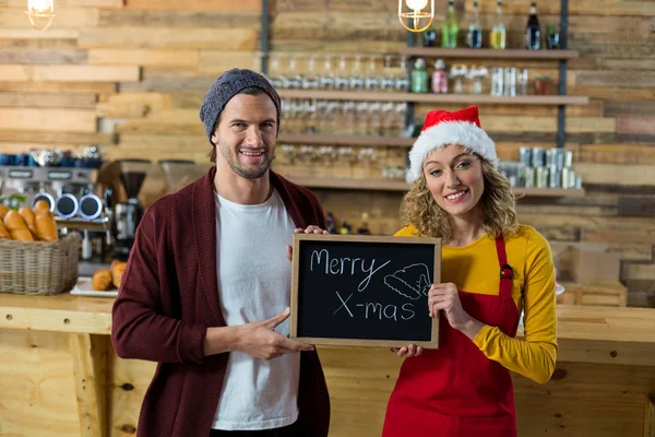 Smiling waitress and owner standing with merry x mas sign board in cafe — Stock Photo, Image