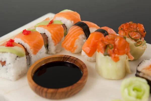 Surtido de sushi servido con salsa de soja sobre pizarra blanca sobre fondo negro —  Fotos de Stock