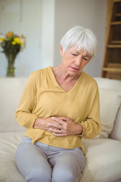 Starší žena trpí bolesti žaludku v obývacím pokoji — Stock fotografie