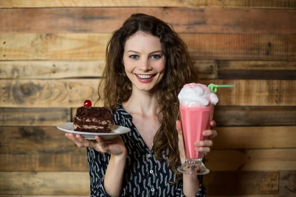 Woman standing with glass of milkshake and pastry in cafe — Stock Photo, Image