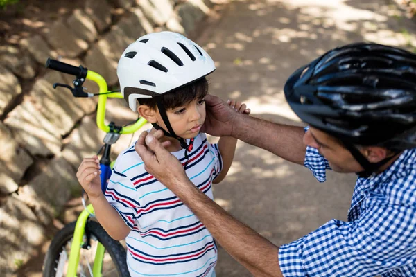 Otec, pomáhá syn v sobě cyklistická přilba v parku — Stock fotografie