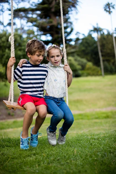 Boy and girl sitting on a swing in park — Stock Photo, Image