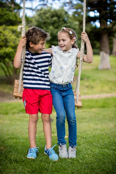 Niño y niña sentados en un columpio en el parque — Foto de Stock