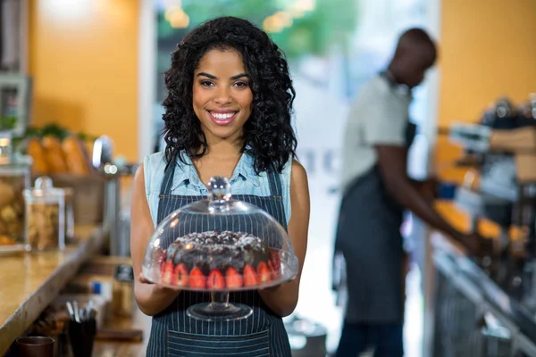 Retrato de camarera sonriente sosteniendo un puesto de pastel con pastel de chocolate — Foto de Stock