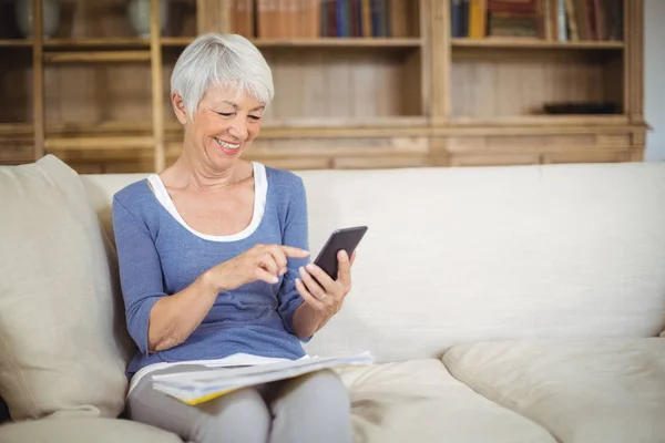 Oudere vrouw die mobiele telefoon gebruikt in de woonkamer — Stockfoto