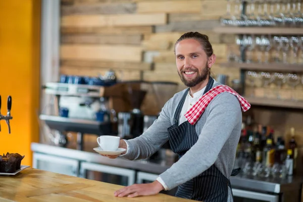 Retrato de garçom sorrindo oferecendo xícara de café — Fotografia de Stock