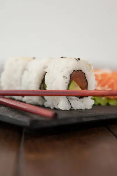 Uramaki et sushi sashimi servis avec des baguettes en ardoise de pierre noire — Photo