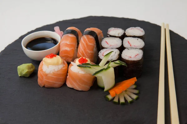 Набор разнообразных суши подается на черном камне с соевым соусом и палочками для еды — стоковое фото