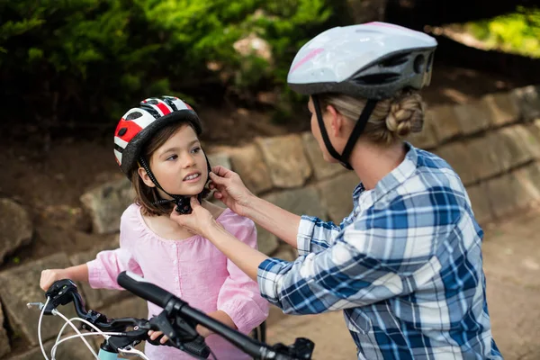 Madre ayudando a su hija a usar casco de bicicleta en el parque — Foto de Stock