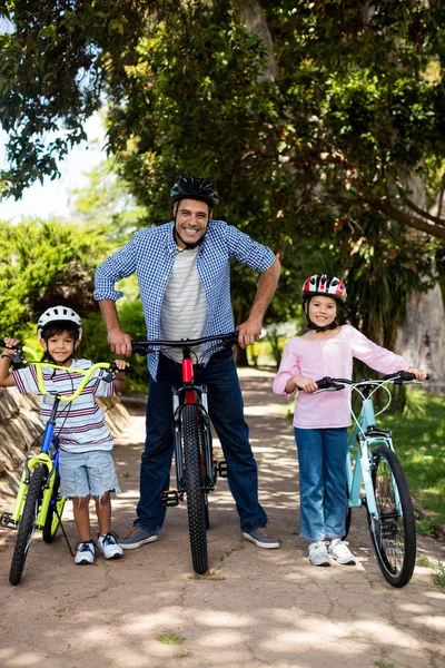 Retrato de pai e filhos de pé com bicicleta no parque — Fotografia de Stock