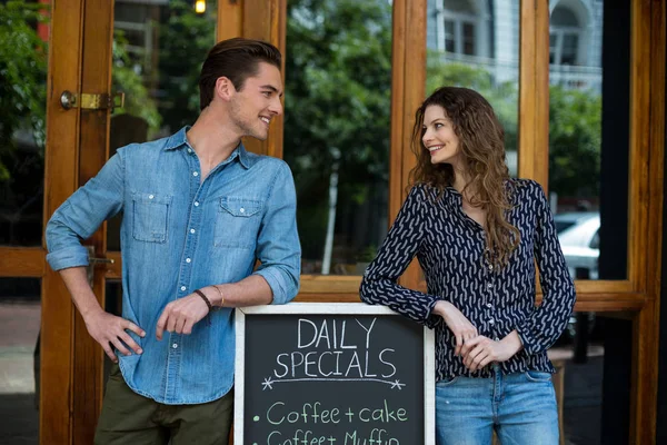 Мужчина и женщина, опирающиеся на меню доски возле кафе — стоковое фото