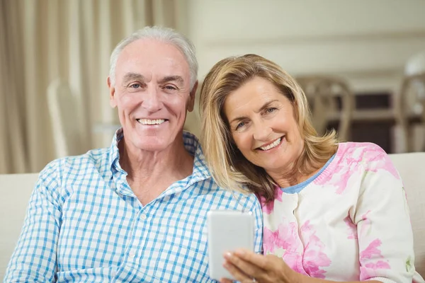 S úsměvem starší pár sedí na pohovce s notebookem v obývacím pokoji — Stock fotografie