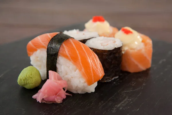 Nigiri och uramaki sushi serveras på svart sten skiffer på träbord — Stockfoto