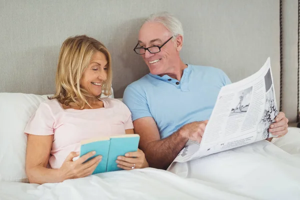 Seniorenpaar liest Zeitung und Buch im Bett — Stockfoto