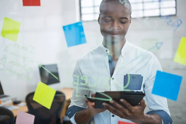 Empresário usando tablet digital enquanto escreve em nota pegajosa — Fotografia de Stock