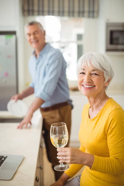 Mulher sênior feliz segurando copo de vinho na cozinha — Fotografia de Stock