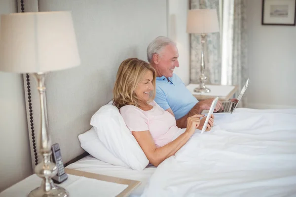 노트북과 디지털 태블릿을 사용 하 여 침대에 행복 한 수석 커플 — 스톡 사진