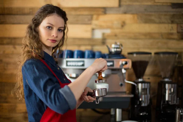 Serveerster een stamper met gemalen koffie in een portafilter drukken — Stockfoto