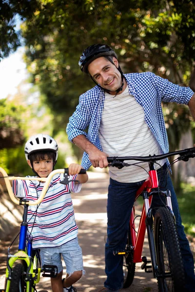 Retrato de pai e filho de pé com bicicleta no parque — Fotografia de Stock
