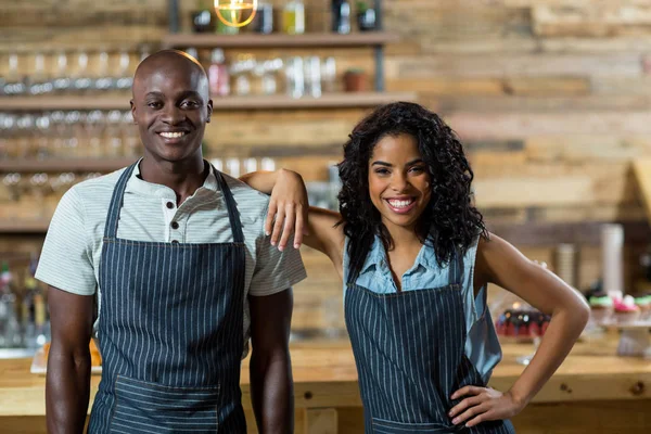 Smiling waiter and waitress standing against counter in cafe — Stock Photo, Image