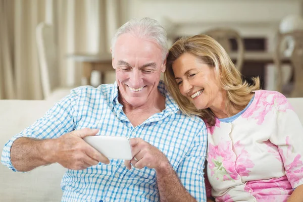 Sorridente coppia di anziani rivedere le foto catturate sul telefono cellulare in soggiorno — Foto Stock