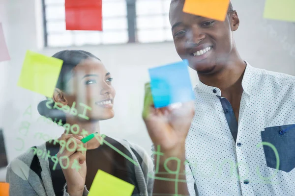 Compañeros de negocios sonrientes escribiendo en notas adhesivas — Foto de Stock