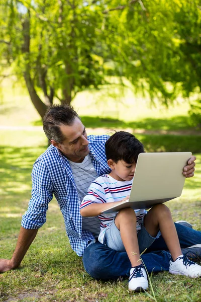 Chłopiec siedzi na kolanach ojców i korzysta z laptopa w parku — Zdjęcie stockowe