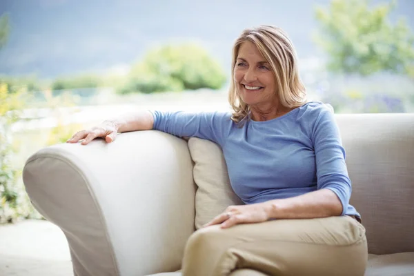 Mujer mayor sonriente sentada en el sofá en la sala de estar —  Fotos de Stock