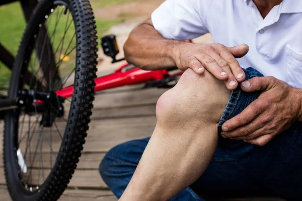 Mid section of fallen cyclist holding his injured knee — Stock Photo, Image
