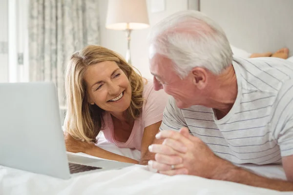 Lächelndes Paar auf dem Bett liegend und mit Laptop — Stockfoto