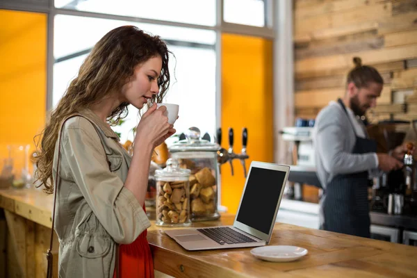 Kobieta stojąc w kasie i przy użyciu laptopa przy kawie — Zdjęcie stockowe